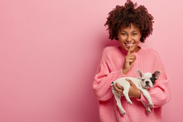 Afroamerikanerfrau, die rosa Pullover hält Welpen hält