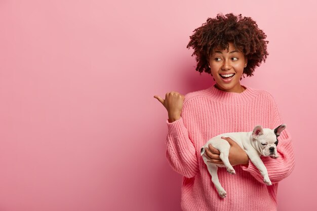 Afroamerikanerfrau, die rosa Pullover hält Welpen hält
