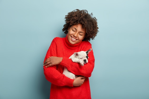 Afroamerikanerfrau, die roten Pullover hält Hund hält