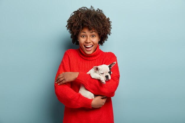 Afroamerikanerfrau, die roten Pullover hält Hund hält