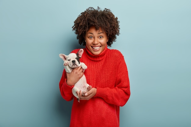 Afroamerikanerfrau, die roten Pullover hält Hund hält