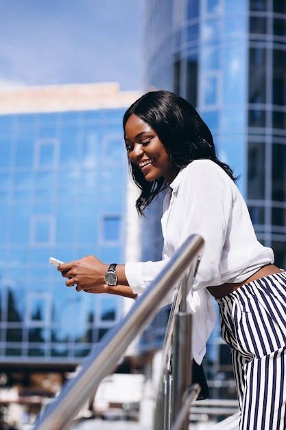 Afroamerikanerfrau draußen durch den Wolkenkratzer mit Telefon