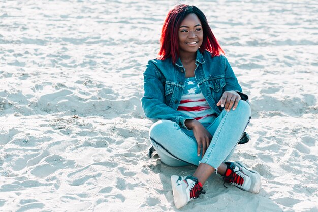 Afroamerikanerfrau mit den Überfahrtbeinen, die auf Sand sitzen