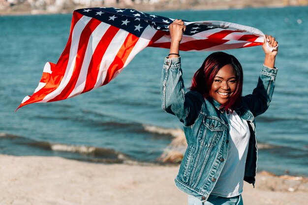 Afroamerikanerfrau, welche die amerikanische Flagge wellenartig bewegt in Wind hält