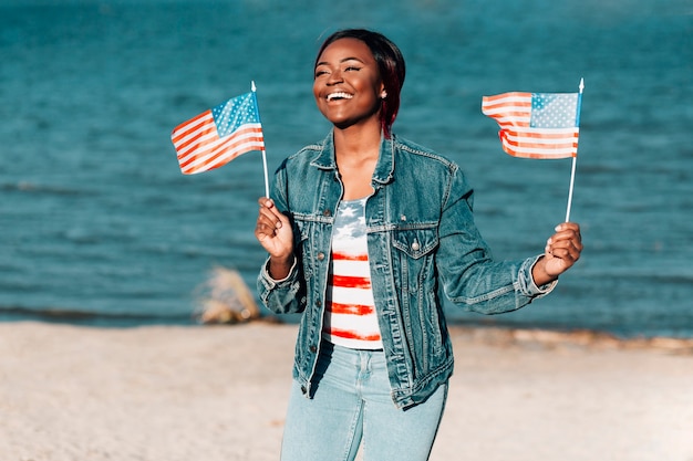 Afroamerikanerfrau, welche die amerikanischen Flaggen stehen auf Küste hält