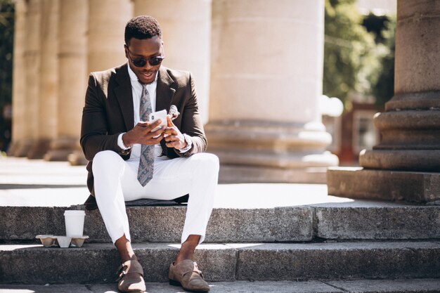 Afroamerikanergeschäft mit dem Kaffee und Telefon, die auf der Treppe eines Gebäudes sitzen