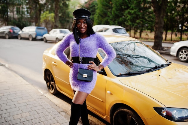 Afroamerikanerin in violettem Kleid und Mütze posierte vor gelbem Auto
