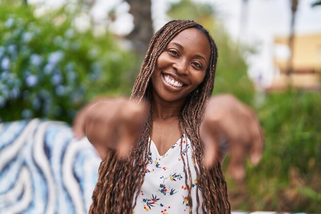 Afroamerikanerin lächelt selbstbewusst und zeigt mit den Fingern auf die Kamera im Park