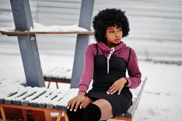Afroamerikanerin mit lockigem Haar posierte am Wintertag auf der Bank sitzend