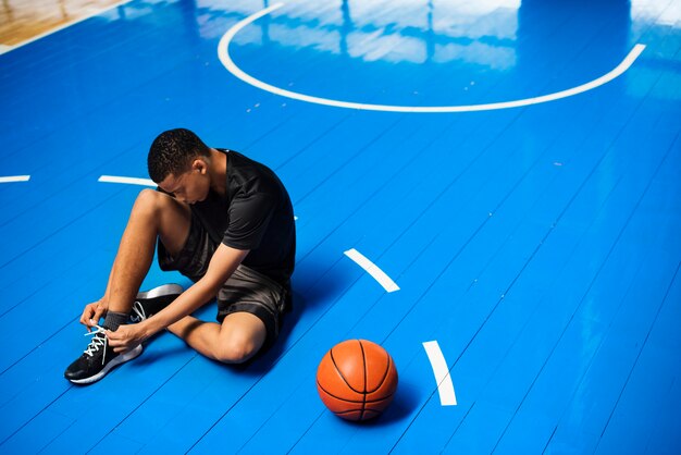 Afroamerikanerjugendlicher, der seine Schnürsenkel auf einem Basketballplatz bindet