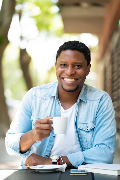 Afroamerikanermann, der einen Kaffee genießt und trinkt, während er draußen im Kaffeehaus sitzt