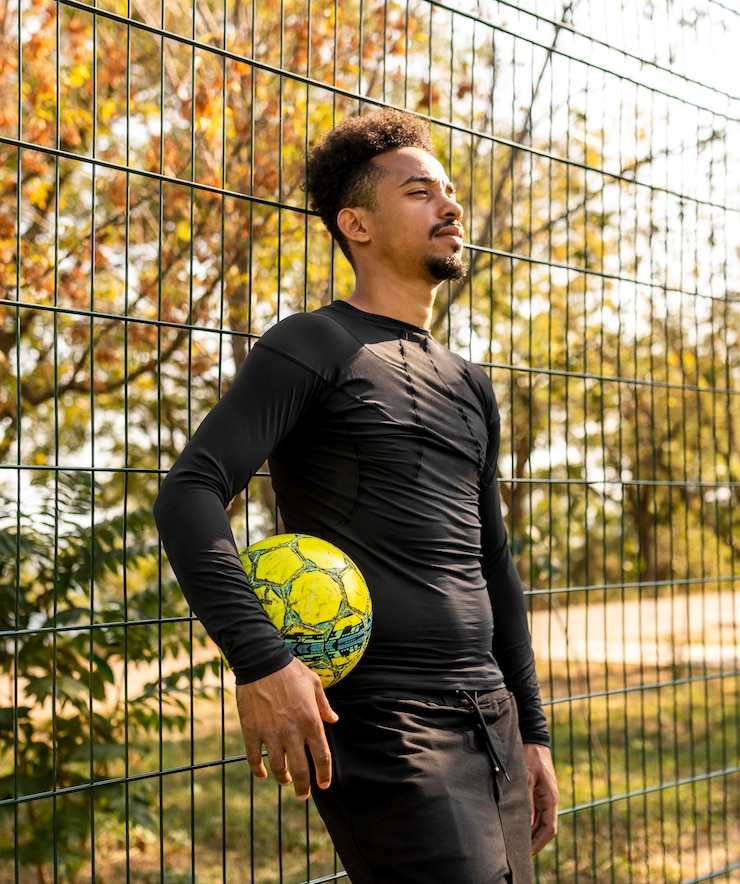 Kostenlose Foto afroamerikanermann, der mit einem fußball auf einem feld aufwirft
