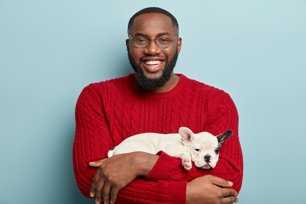 Afroamerikanermann, der roten pullover trägt und kleinen hund hält