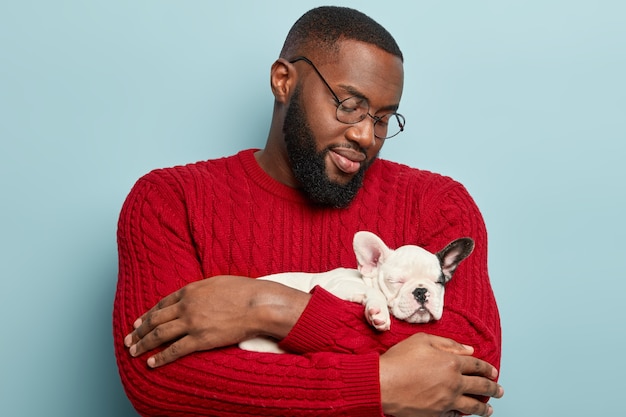 Afroamerikanermann, der roten Pullover trägt und kleinen Hund hält