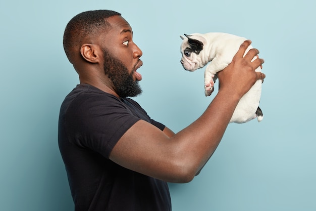 Afroamerikanermann, der schwarzes T-Shirt trägt und kleinen Hund hält