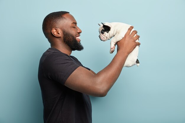 Afroamerikanermann, der schwarzes T-Shirt trägt und kleinen Hund hält