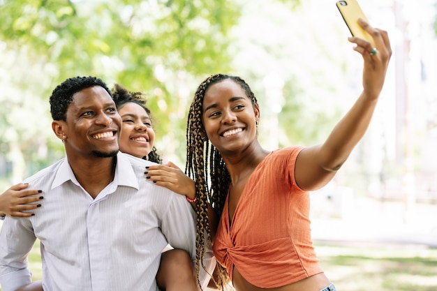 Afroamerikanische Familie, die Spaß hat und einen Tag im Park genießt, während sie zusammen mit einem Mobiltelefon ein Selfie macht.