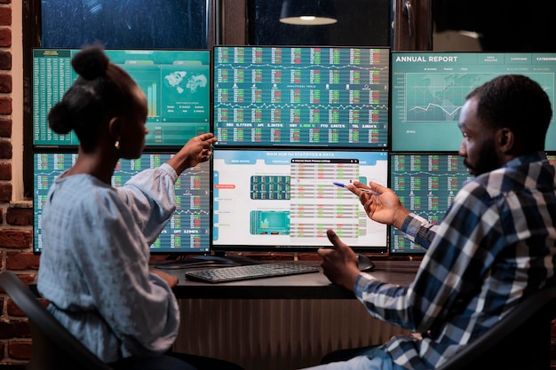 Kostenloses Foto afroamerikanische finanzberater überprüfen marktdaten und statistiken in echtzeit, um aktien zu verkaufen. hedgefonds-händler sitzen an einer workstation und zeigen auf ein display mit live-index-charts.