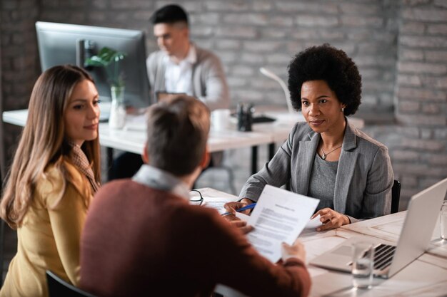 Afroamerikanische Finanzberaterin geht mit ihren Kunden den Papierkram durch, während sie ein Meeting im Büro hat