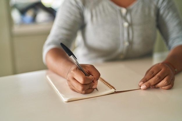 Afroamerikanische Frau schreibt auf Notizbuch und sitzt zu Hause am Tisch