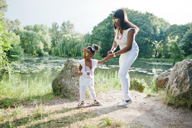 Afroamerikanische Mutter mit Tochter am weißen Kleiderhintergrundsee am Park