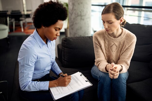 Afroamerikanische Psychotherapeutin schreibt Notizen während einer Sitzung mit ihrer Patientin