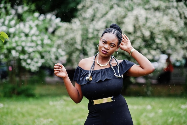 Afroamerikanische Ärztin im schwarzen Kleid mit Stethoskop posierte im Freien unter Regen