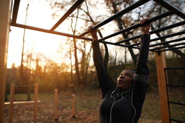 Afroamerikanische Sportlerin, die im Outdoor-Fitnessstudio im Park horizontale Balken überquert