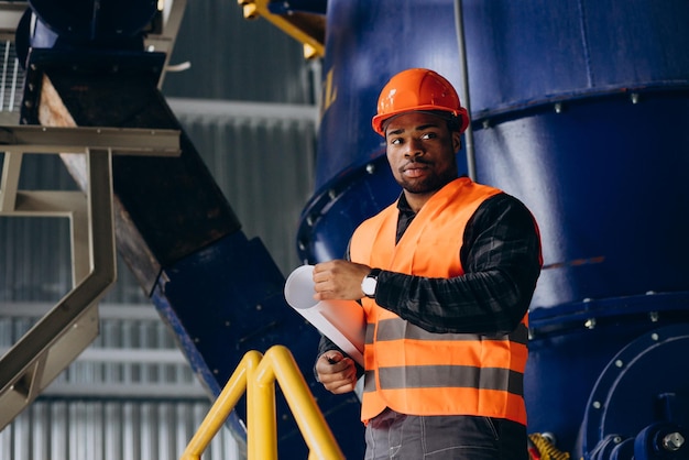 Afroamerikanischer Arbeiter, der in Uniform mit Sicherheitshut in einer Fabrik steht