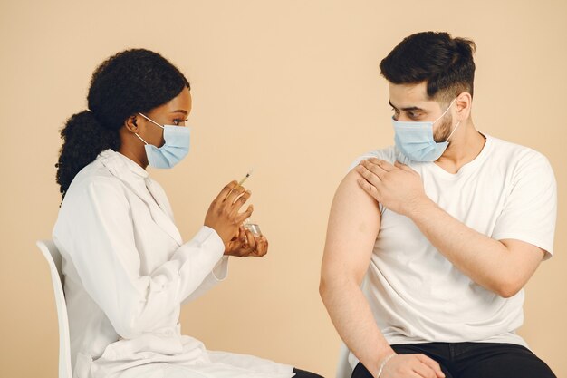 Afroamerikanischer Arzt, der einem Mann einen Impfstoff verabreicht. Beide tragen Masken, isoliert. Covid-19-Impfung.