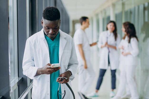 Afroamerikanischer Arztmann, der das Smartphone im Korridor des Krankenhauses benutzt
