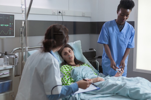 Afroamerikanischer Assistent legt Oximeter auf Finger und überprüft Herzschlagpuls während des Erholungstermins ...