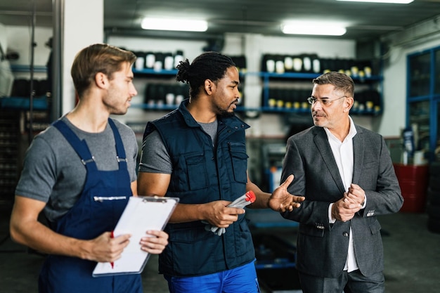 Afroamerikanischer Automechaniker und sein Mitarbeiter kommunizieren mit ihrem Manager in der Werkstatt