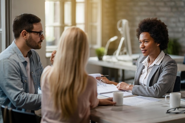 Afroamerikanischer Bankmanager im Gespräch mit einem Ehepaar, während er deren Geschäftsberichte im Büro analysiert