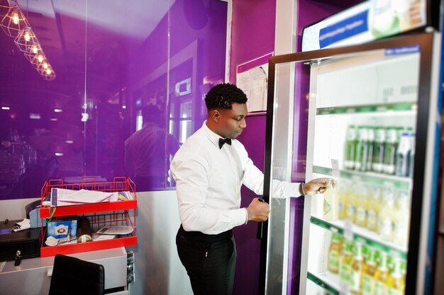 Afroamerikanischer Barkeeper an der Bar, der Bier aus dem Kühlschrank nimmt