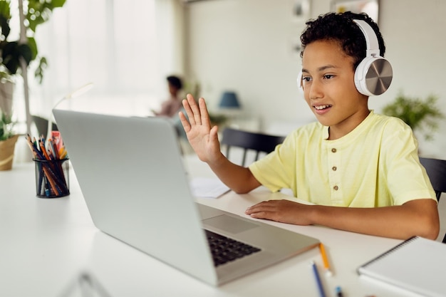 Kostenloses Foto afroamerikanischer junge benutzt laptop und winkt während des videoanrufs beim homeschooling