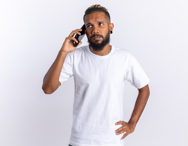 Afroamerikanischer junger Mann im weißen T-Shirt, der beim Telefonieren verwirrt aussieht
