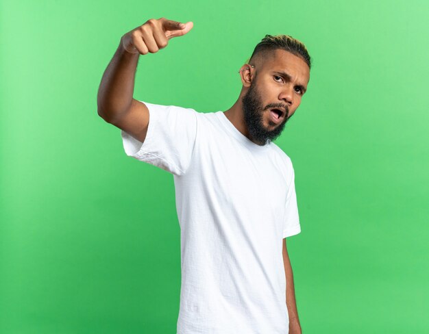 Afroamerikanischer junger Mann im weißen T-Shirt, der mit dem Zeigefinger auf die Kamera zeigt, die wütend ist