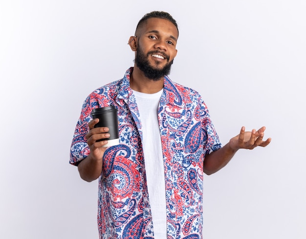 Afroamerikanischer junger Mann in buntem Hemd, der in die Kamera schaut, fröhlich lächelnd mit Pappbecher über Weiß