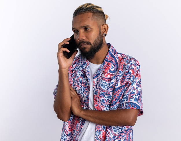Afroamerikanischer junger Mann in buntem Hemd traurig und verwirrt beim Telefonieren mit dem Handy