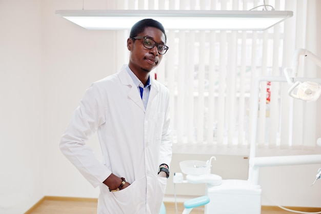 Afroamerikanischer männlicher Arzt mit Brille, der in der Nähe des Zahnarztstuhls in der Zahnklinik steht