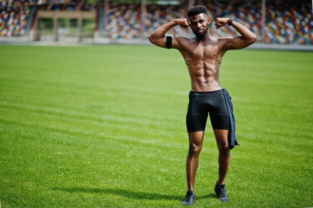 Afroamerikanischer männlicher Athlet sexy Sport mit nacktem Oberkörper Mann mit laufendem Sportarmgehäuse für Handy posierte auf grünem Gras des Fußballstadions