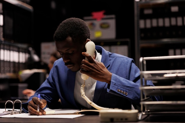 Afroamerikanischer Manager spricht über ein Festnetztelefon, diskutiert Managementforschung mit einem Fernbuchhalter im Lagerraum.