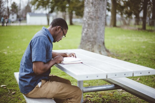 Afroamerikanischer Mann, der an einem Tisch sitzt und die Bibel liest