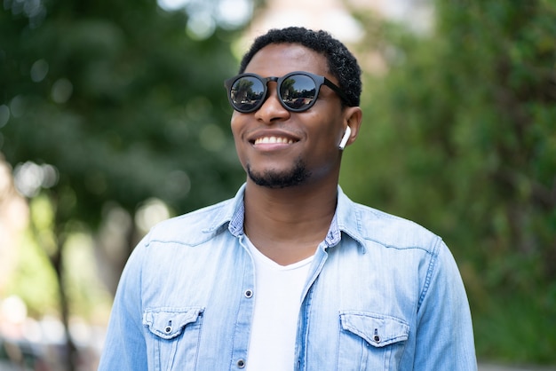 Afroamerikanischer Mann, der eine Sonnenbrille trägt und lächelt, während er im Freien im Park steht
