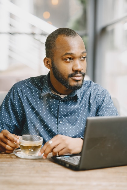 Afroamerikanischer Mann, der hinter einem Laptop arbeitet. Mann mit Bart sitzt in einem Café und trinkt einen Tee.