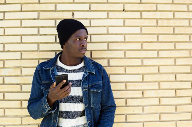 Afroamerikanischer Mann mit Smartphone vor Wand