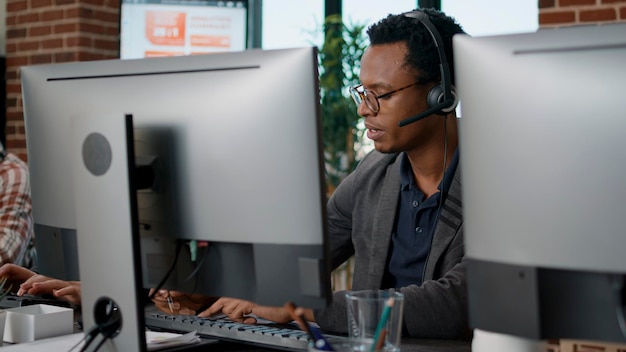 Afroamerikanischer Mitarbeiter, der ein Headset im Kundenservice verwendet und einen Anruf über Telemarketing-Verkäufe beantwortet. Männlicher Operator, der im Call-Center-Büro arbeitet, um Kunden in der Hotline zu helfen.