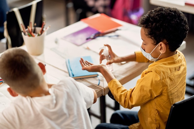 Afroamerikanischer Schüler, der im Klassenzimmer Händedesinfektionsmittel verwendet