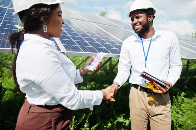 Afroamerikanischer Techniker überprüft die Wartung der Sonnenkollektoren Eine Gruppe von drei schwarzen Ingenieuren trifft sich in der Solarstation und macht einen Deal mit Geld